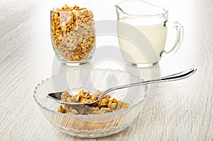 Glass with granola, pitcher with yogurt, spoon and muesli in bowl on wooden table