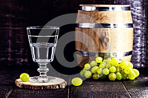 Glass of Grappa on wooden background with old oak barrel, grape-based drink, distilled. Selective focus