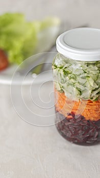 Glass with grated beetroot, carrot and cucumber and a plate on background