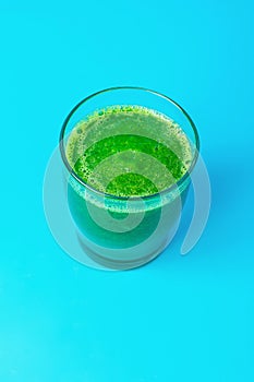 Glass with Green Fresh Raw Smoothie from Leafy Greens Vegetables Fruits Spinach Apples Bananas Kiwi Zucchini on Blue Background