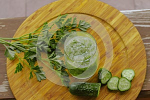 A glass of green healthy juice with cucumbers and parsley leaves on a wooden background close-up selective focus