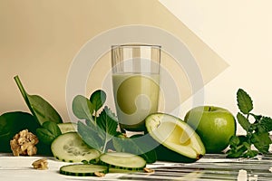 A glass of green juice is on a table with a variety of fruits and vegetables