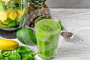 Glass of green smoothie with fresh juicy fruits, spinach, avocado, chia seeds and blender for making healthy detox drink