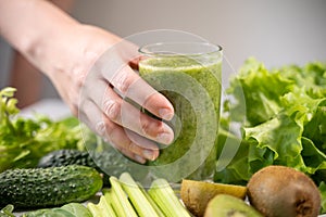 A glass with a green smoothie made from vegetables and fruits. A woman& x27;s hand holds a glass and wants to drink. Healthy