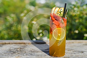 Glass of green tropical tea with lime, orange, watermelon and apple against green summer background