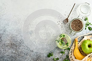 Glass of healthy green smoothie and ingredients for smoothie, fresh spinach, chia seed, pea microgreens, banana, kiwi and apple in