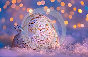 Glass heart on a snow and toned blurred color background of glittering bokeh with glowing lights. New year decoration. Copy space