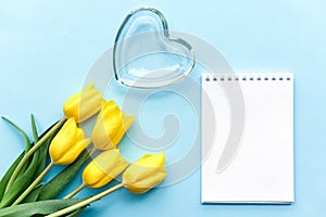 Glass heart and yellow tulips on a blu background, fragile love background, valentines day concept