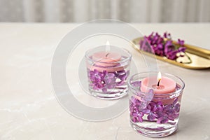 Glass holders with water, lilac flowers and  candles on light table, space for text