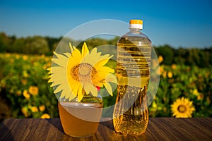 Glass honey jar and bottle of oil on wooden stand with sunflowers field background.