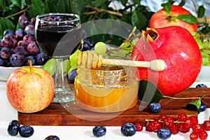 Glass honey jar, fresh ripe apples, pomegranate and other fruits and berries on the table for Jewish New Year - Rosh Hashanah