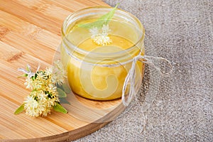 Glass honey jar with linden flowers on a  wooden board