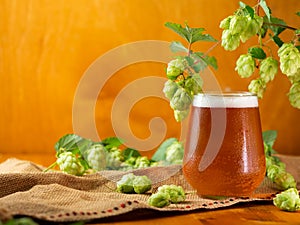 glass of hopped beer or IPA on a wooden table with hop cones