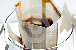 Glass with hot drip coffee bag closeup. Instant paper macro sachet with condensation water drops detail. Fresh morning