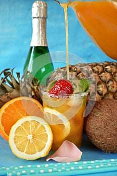 Glass with ice is being filled up with an orange drink surrounded by fruits