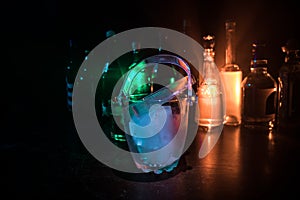 Glass ice bucket on blurred alcohol bottles background with lights and smoke. Club drinks concept. Club bar desk. Ready to serve.