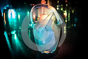 Glass ice bucket on blurred alcohol bottles background with lights and smoke. Club drinks concept. Club bar desk. Ready to serve.