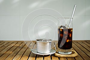 Glass of Ice coffee & Vietnamese traditional coffee filter on wooden table in day light