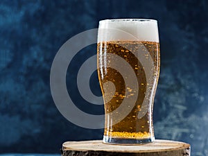 A glass of ice-cold light lager beer with water drops on dark background close-up