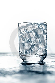 Glass of Ice cube on wooden table and light blurred background