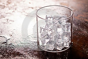 Glass of Ice cube on wooden table and light blurred background