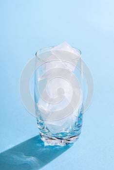 Glass with ice cubes on blue background. Empty glass with ice