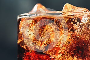 Glass with ice cubes and bubbles of fresh carbonated cola soda drink, macro photo close up