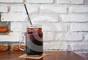 Glass iced black coffee in jar on the wood table with wall brick background