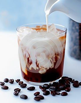 A glass of iced coffee with cream pouring over on light background.