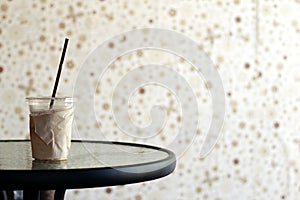 A glass of iced coffee on a glass table with a brown wall background
