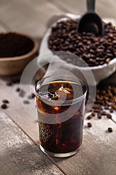 Glass of Iced coffee with ingredients, espresso, whole roasted beans, scoop, grind, bag on wood