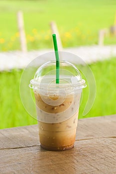 glass of iced coffee on wooden balcony with green nature background