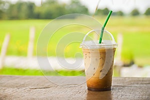 glass of iced coffee on wooden balcony with green nature background