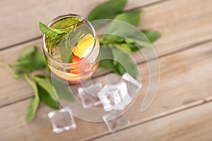 A glass of iced lemon mixed fruit tea with fresh mint leaves and ice cubes scattered on the table