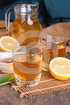 A glass of iced tea with mint and lemon on a wooden table.A glass cup of tea with lemon, mint, and honey on a wooden rustic table