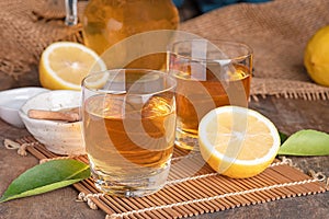 A glass of iced tea with mint and lemon on a wooden table.A glass cup of tea with lemon, mint, and honey on a wooden rustic table