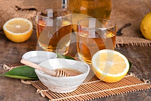 A glass of iced tea with mint and lemon on a wooden table.A glass cup of tea with lemon, mint, and honey on a wooden rustic table