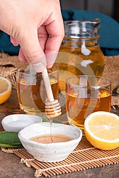 A glass of iced tea with mint and lemon on a wooden table.A glass cup of tea with lemon, mint, and honey on a wooden rustic table