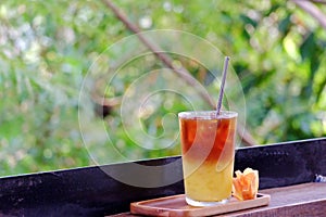 A glass of iced tea soft drink in a wooden tray with an orange flower on wood balcony