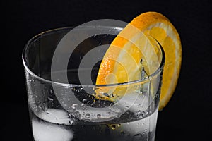 Glass of iced water with an orange slice isolated on a black background