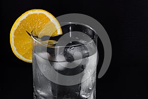 Glass of iced water with an orange slice isolated on a black background