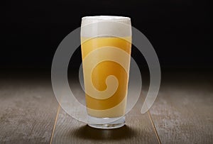 A glass of India Pale Ale, hazy unfiltered juicy draft beer on wooden surface and black background