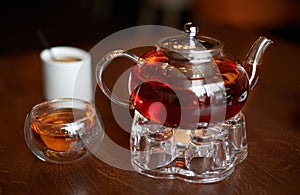 Glass infuser teapot with tea on the trivet and tea cup