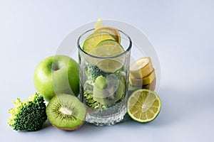 Glass with Ingredients for Fresh Green Smoothie with Kiwi Broccoli Green Apples Babanas and Lime Healthy Detox Blue Background