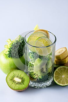 Glass with Ingredients for Fresh Green Smoothie with Kiwi Broccoli Green Apples Babanas and Lime Healthy Detox Blue Background