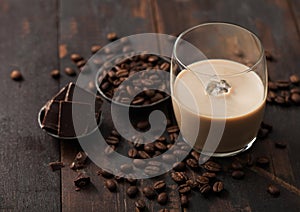 Glass of Irish cream baileys liqueur with coffee beans and dark chocolate in steel bowl on dark wood background