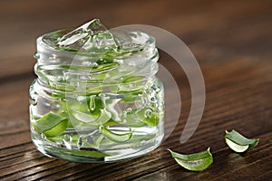 Glass jar of aloe vera gel, slice of aloe leaves on a wooden board. Natural remedy