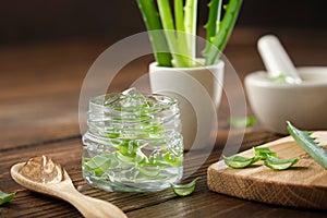 Glass jar of aloe vera gel, sliced aloe plant on a cutting board. Mortars of aloe vera leaves on background.