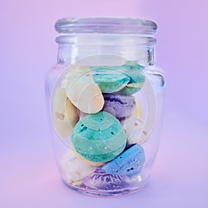 Glass jar, beach stones or rocks on table in studio isolated on a purple background. Beauty, art and variety of colorful