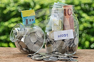 glass jar bottle labeled as house with full of coins and miniature house on as home, property or mortgage investment concept